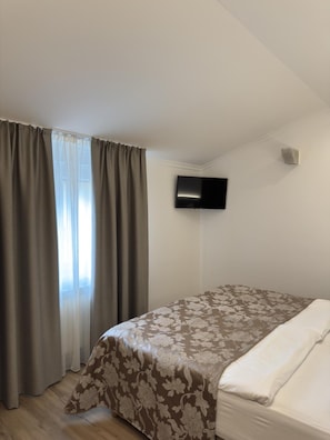 A hotel room with a bed, curtains, a television mounted on the wall, and a window with curtains.