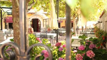 An outdoor café with tables and chairs, surrounded by greenery and flowers.