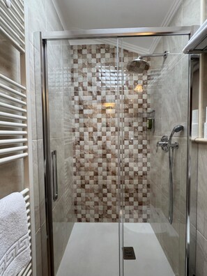 A walk-in shower with a glass door, checkered tile wall, and a handheld showerhead.
