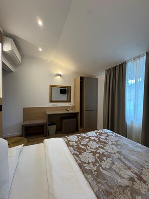 A hotel room with a bed, a desk, a wardrobe, a mirror, and a window with curtains.