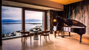 Un piano de cola en una habitación amplia con un gran ventanal que ofrece una vista panorámica de montañas y agua.
