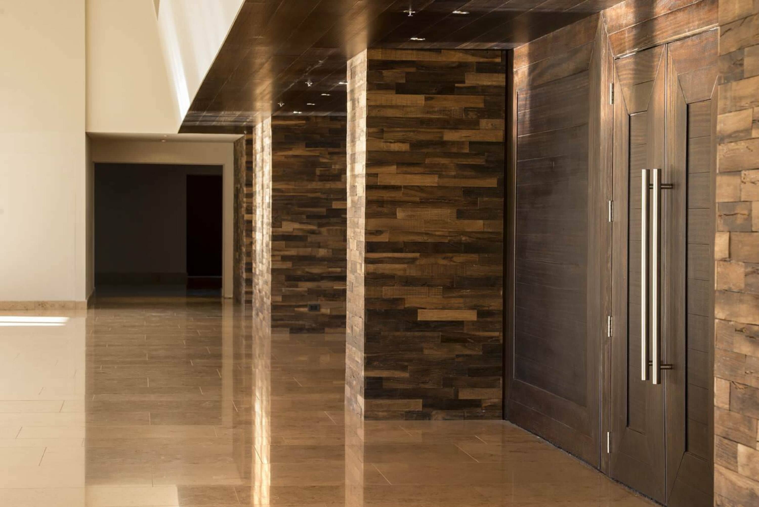 A hallway with a polished floor, wooden wall panels, and a door with a metallic handle.