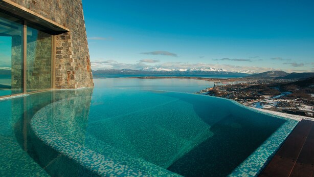 Una piscina infinita con vistas despejadas a montañas y un cuerpo de agua.