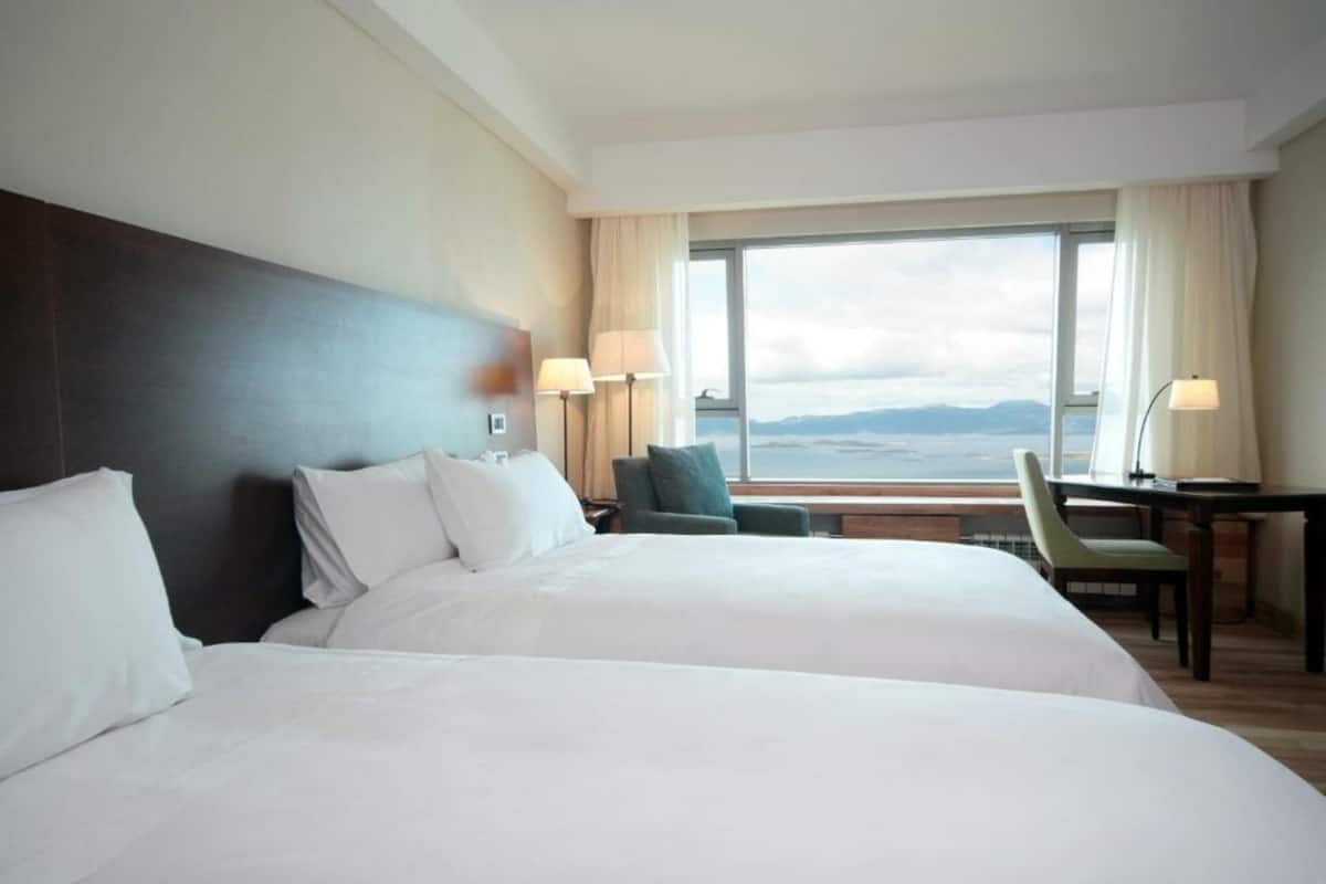 Habitación de hotel con dos camas, un escritorio y vista al mar.