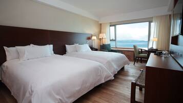 A hotel room with two beds, a desk, and a view of the sea.
