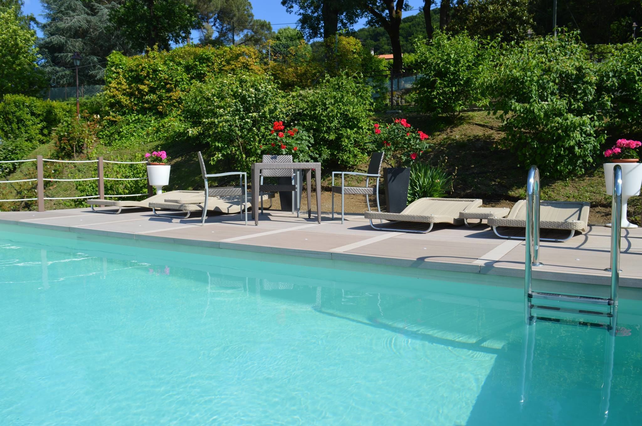 A swimming pool with lounge chairs and a table, surrounded by greenery and flowers.