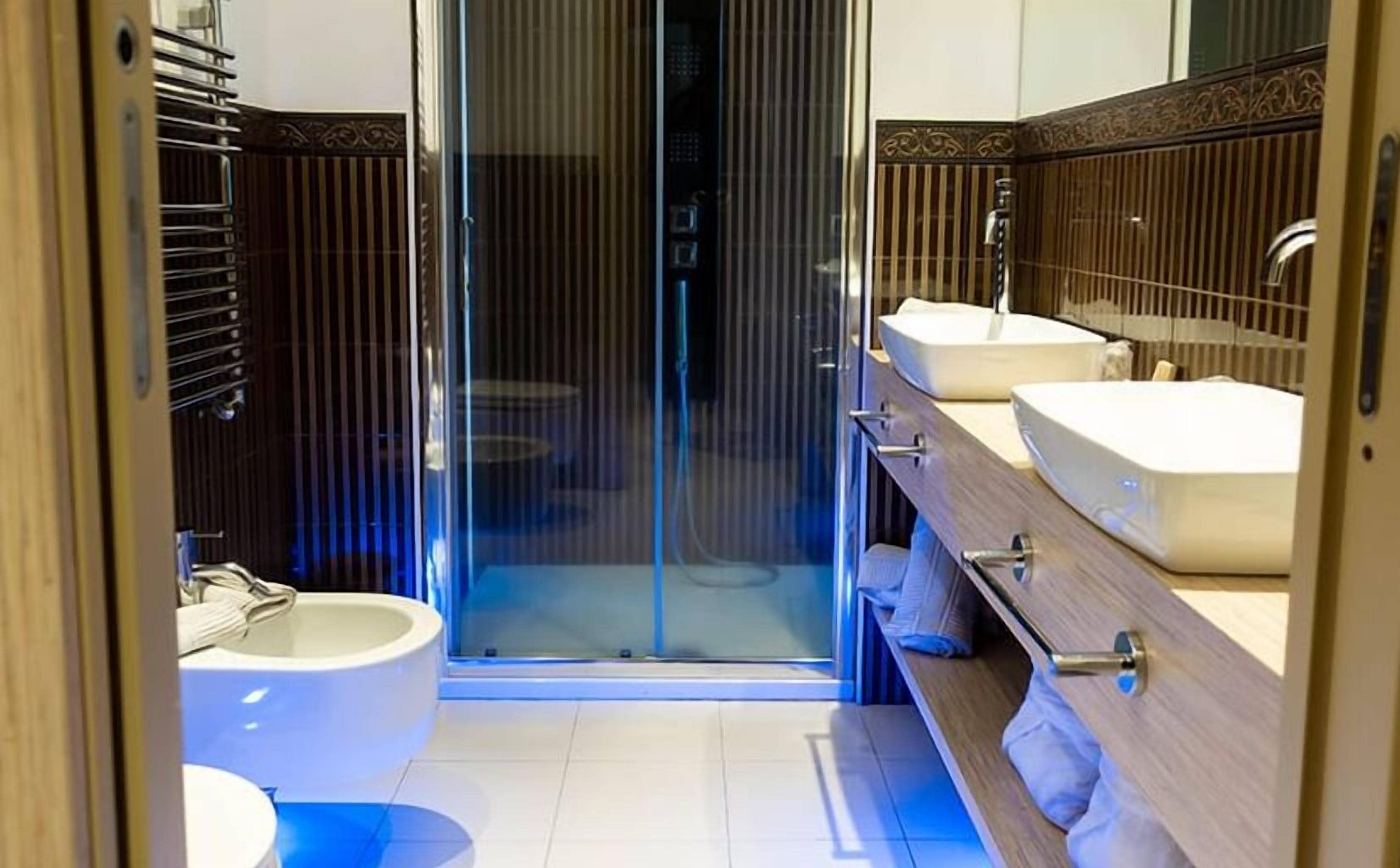 A modern bathroom with a glass shower enclosure, a toilet, and two sinks.