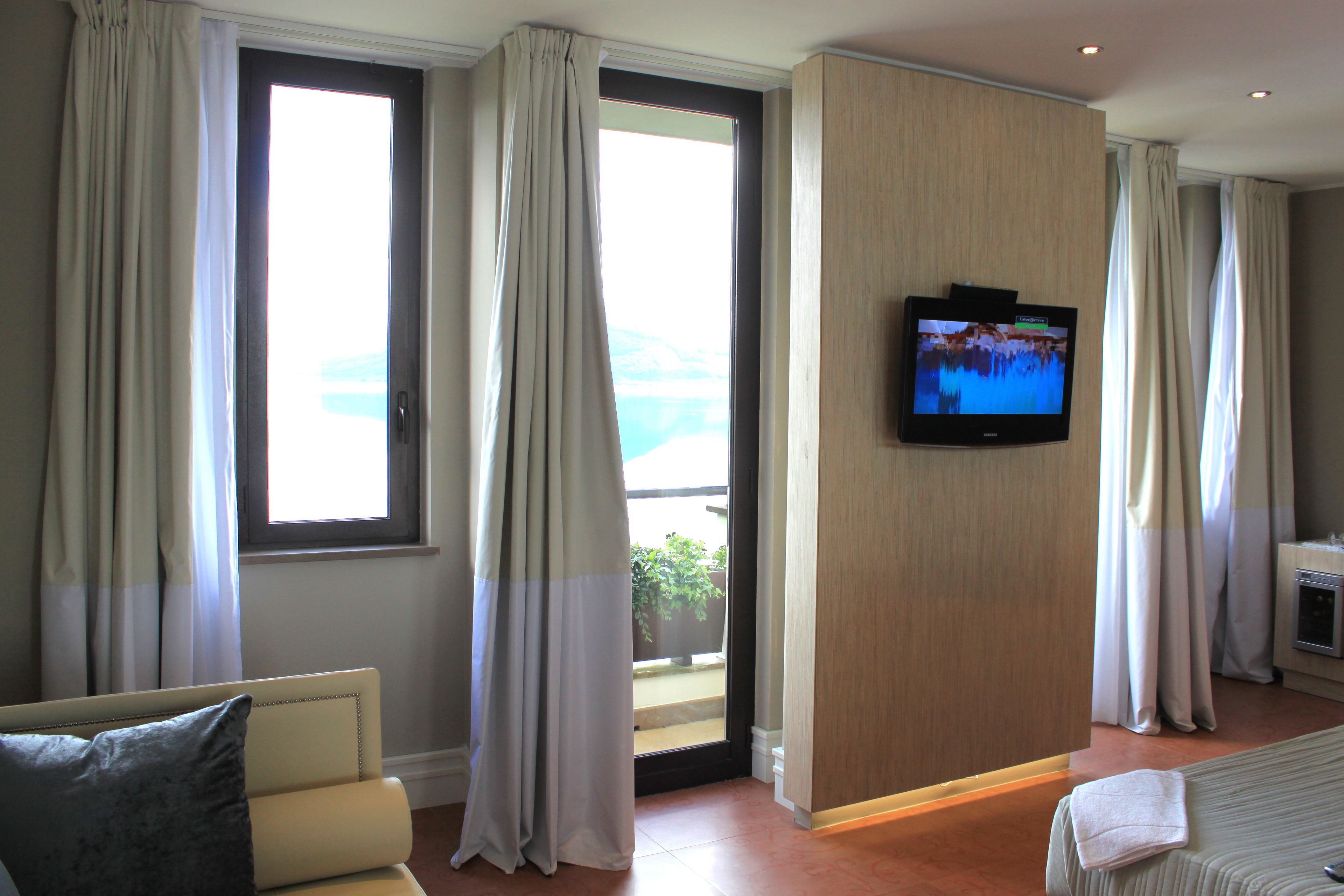 Habitación de hotel con cama, televisión montada en la pared y vistas al exterior a través de un ventanal grande.
