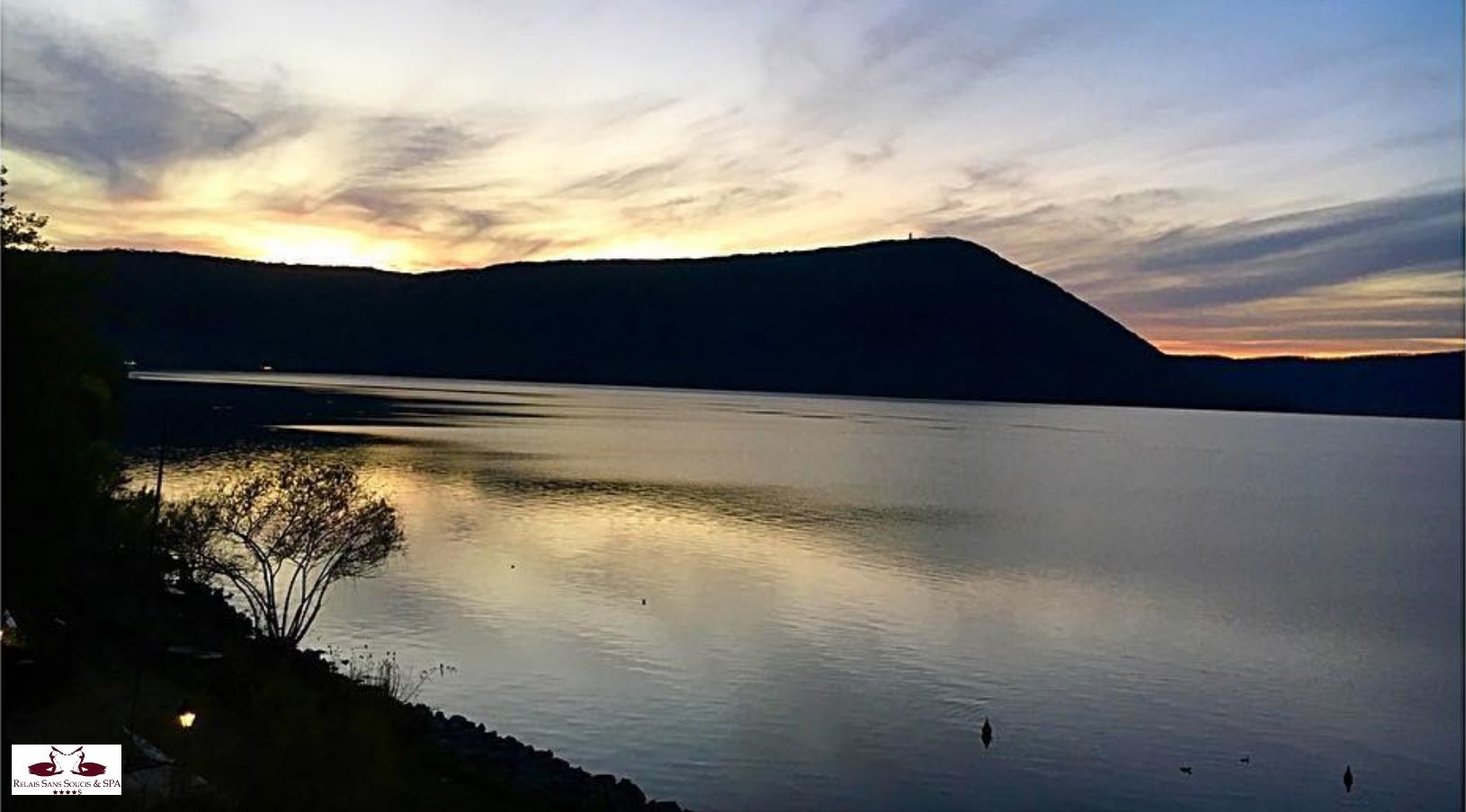 A calm lake at sunset with a silhouette of a hill in the background.