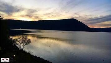 A calm lake at sunset with a silhouette of a hill in the background.