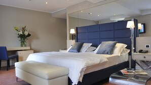 A modern hotel room with a large bed, a desk, a chair, a bedside table, and a mirror. - Relais Sans Souci and Spa (Ronciglione)