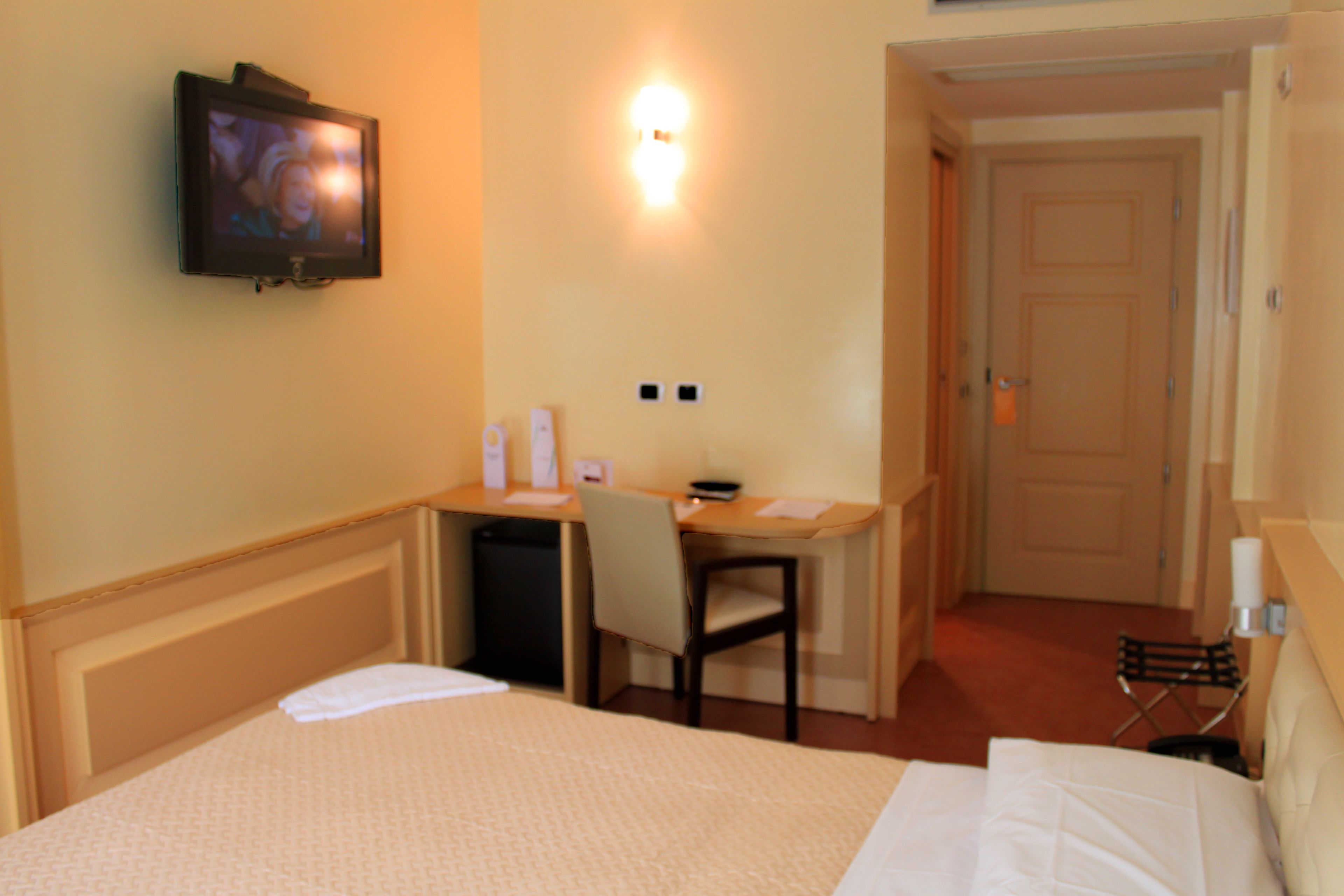 Una habitación de hotel con cama, escritorio, silla, televisor y puerta.