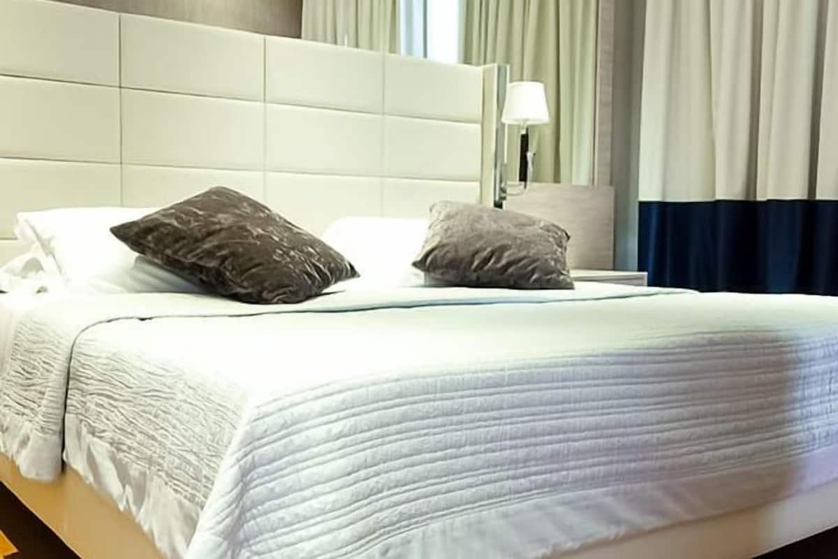 A hotel room with a large bed, white bedding, and a headboard.