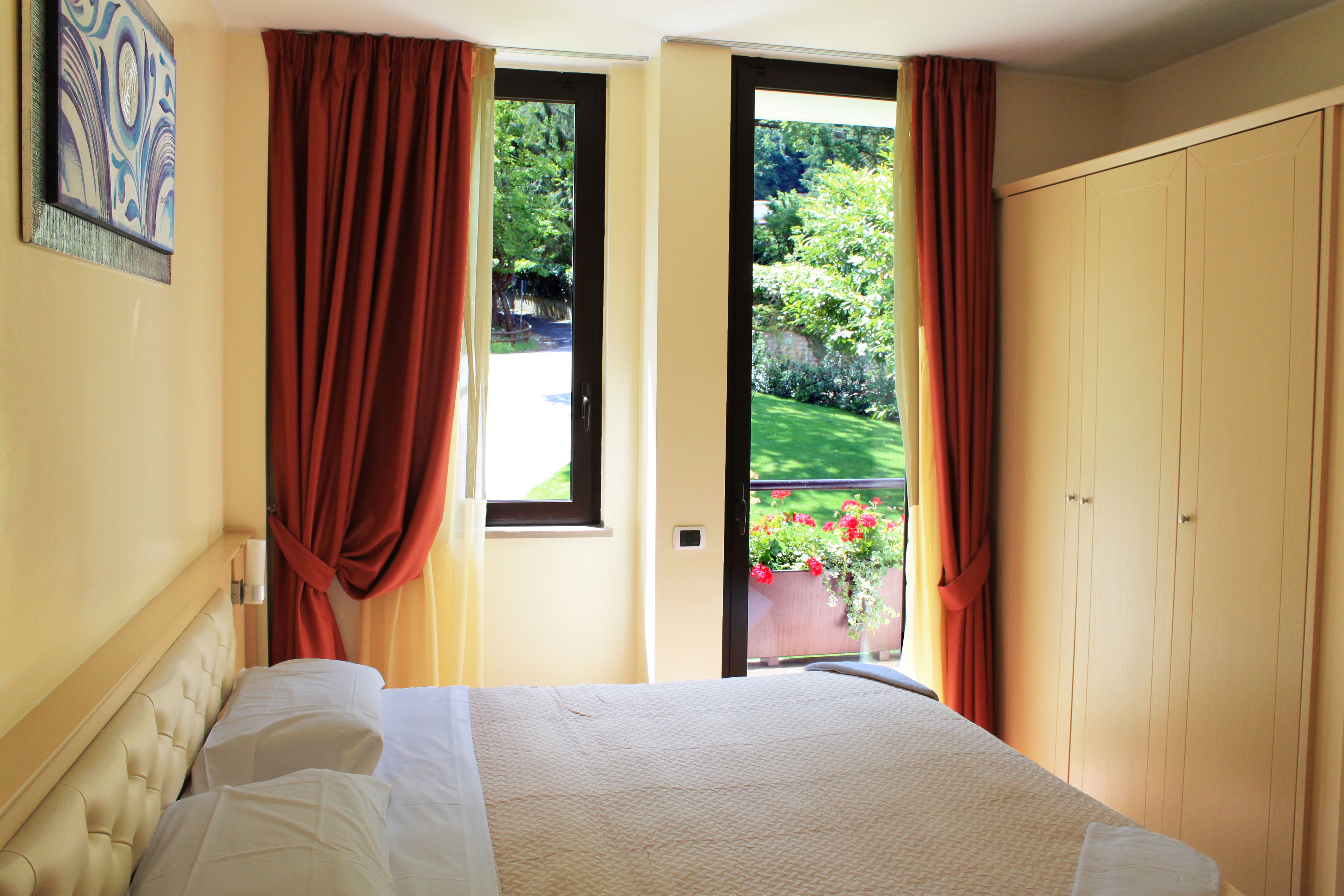 A bedroom with a bed, a window, and a view of a garden.