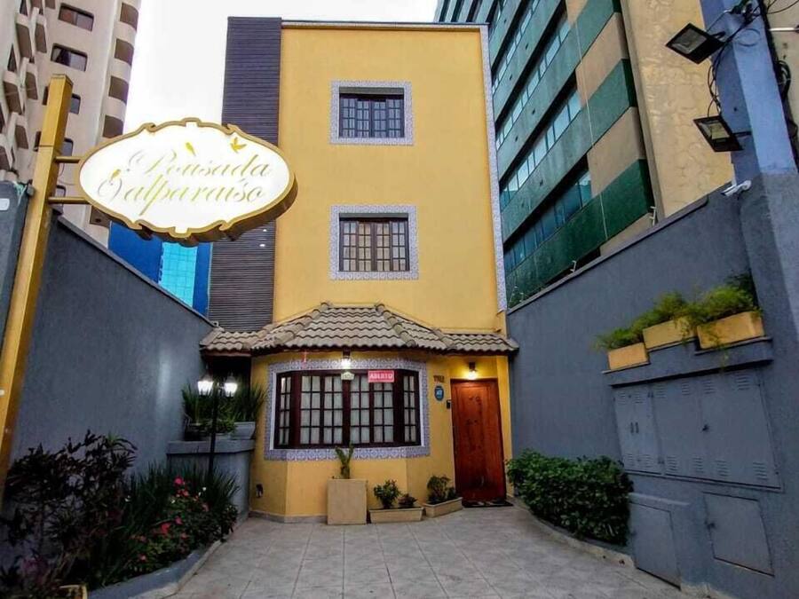 Un edificio con fachada amarilla, una pequeña entrada con techo de tejas y un cartel que dice "Pensão Balparaiso".
