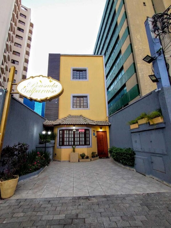 A building with a yellow facade, a small entrance with a tiled roof, and a sign that reads "Pensão Balparaiso". - Hotel Valparaiso (São Paulo)
