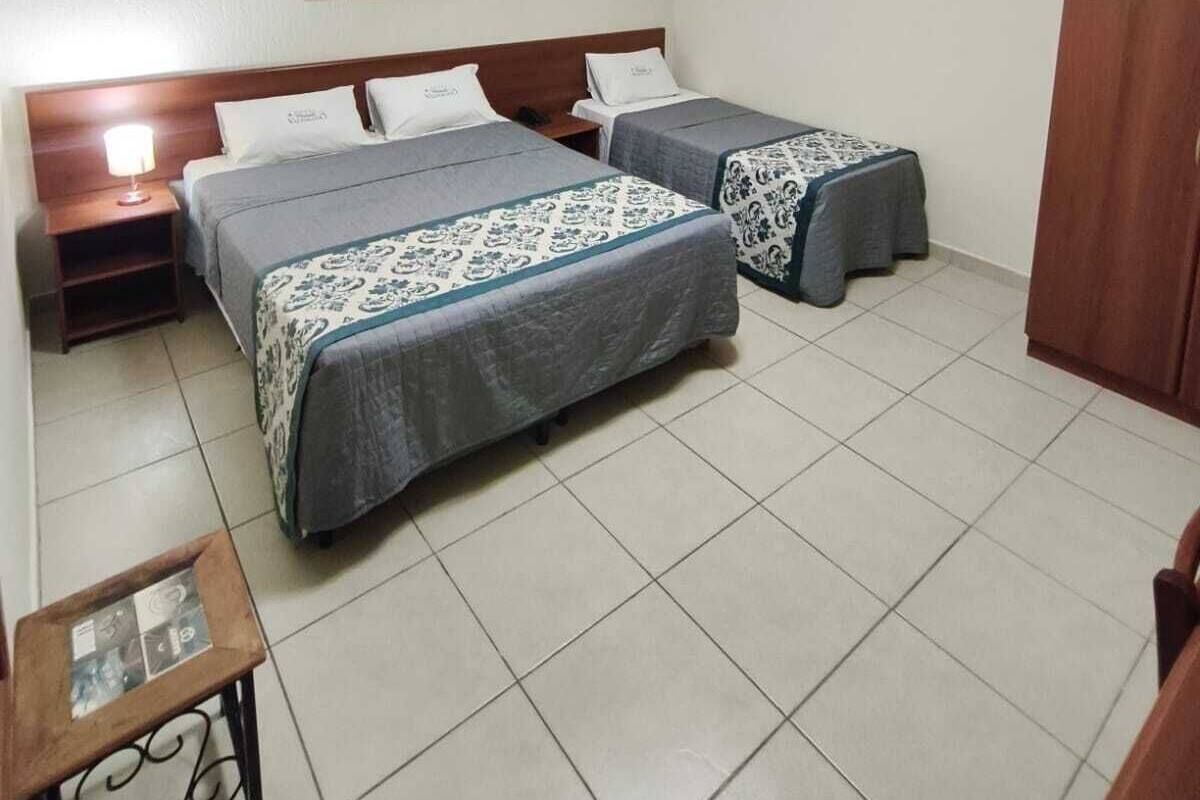 A hotel room with two beds, a wooden headboard, a small table with a lamp, and a wardrobe.