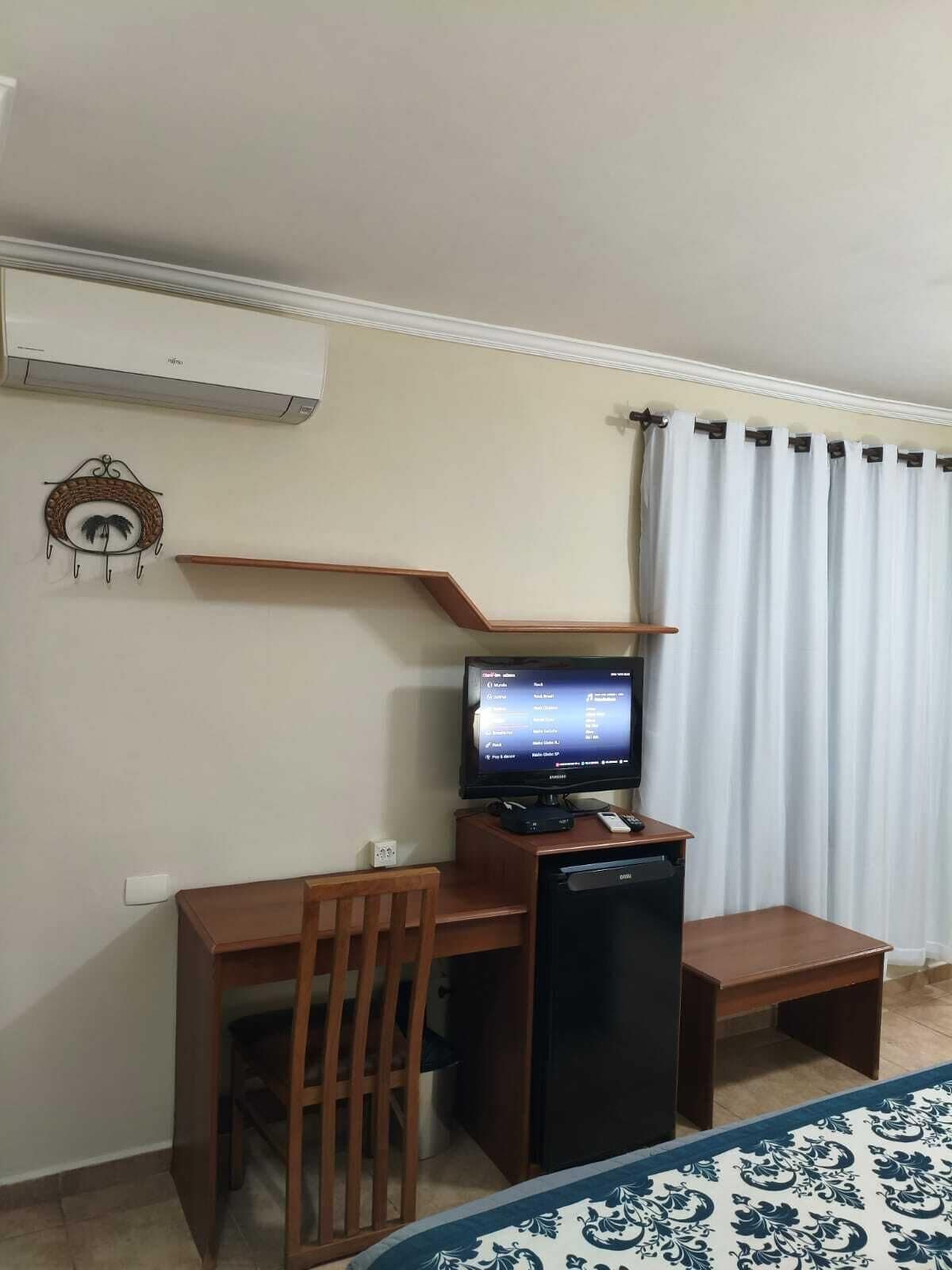 Een kamer met een bureau, stoel, televisie en een kleine koelkast.