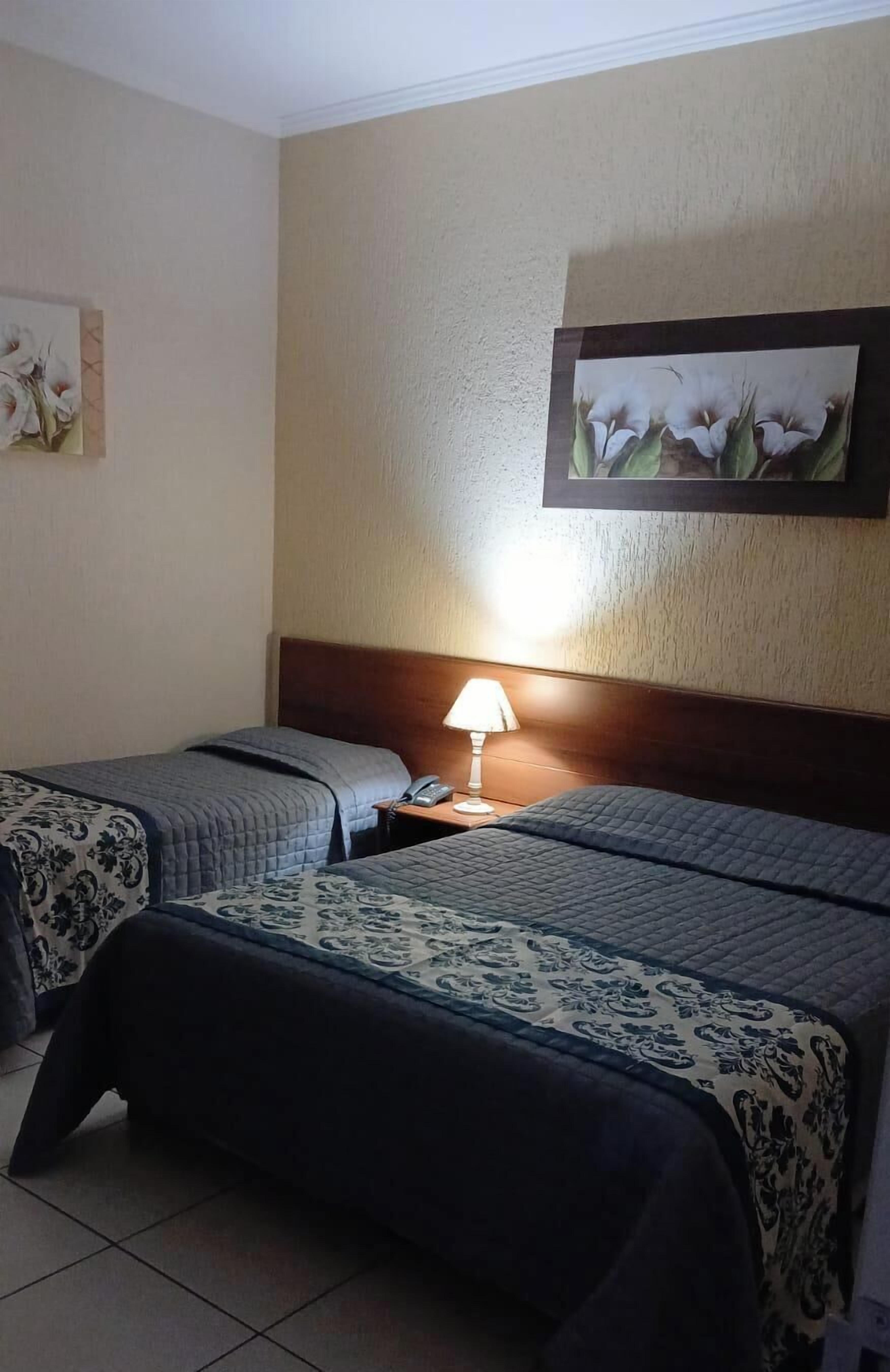 Habitación de hotel con dos camas, una mesita de noche con lámpara y un cuadro en la pared.