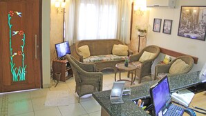 Una sala de estar con sofá, sillas, televisión, laptop y escritorio.