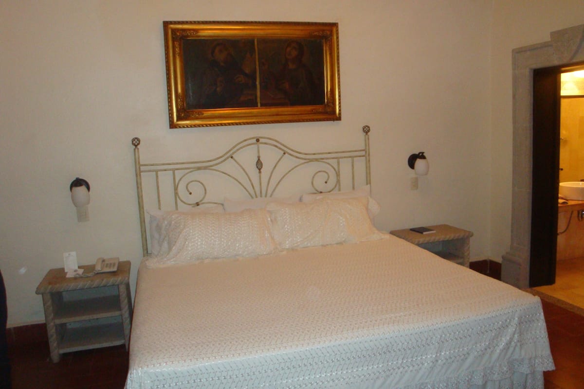 A neatly made bed with a white bedspread, a nightstand with a telephone, and a painting above the bed.