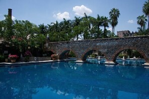 Una piscina con un puente de piedra, rodeada de palmeras y follaje.