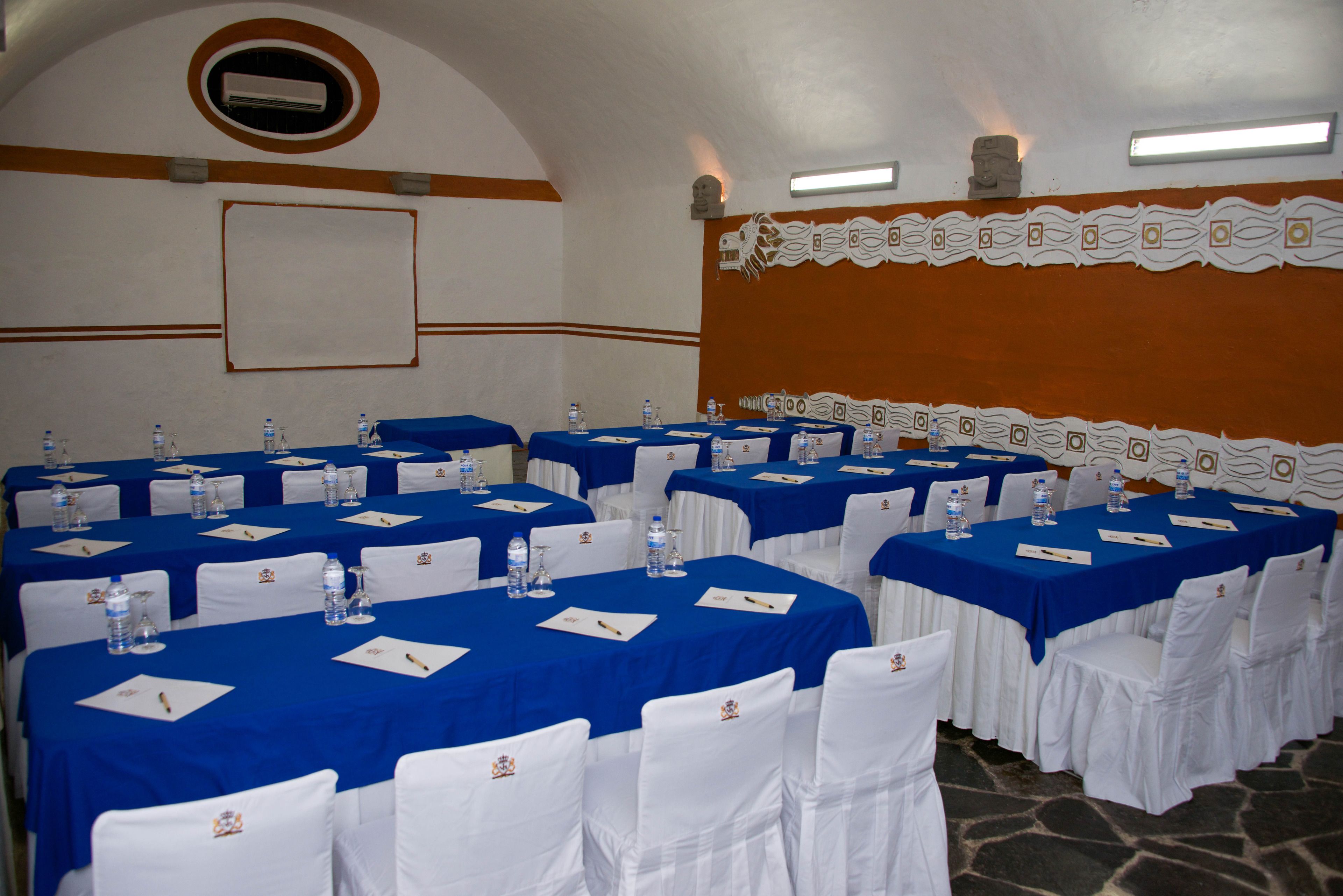 Un salón de conferencias con varias mesas, sillas blancas y manteles azules.