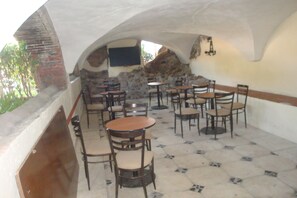 Un patio exterior con paredes de piedra, varias mesas y sillas, y un televisor de pantalla plana montado en la pared.