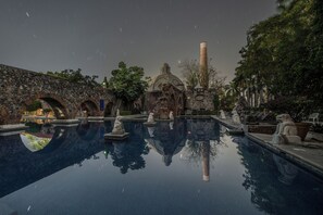 Un área de piscina tranquila con estatuas de piedra, un puente de piedra y una estructura en forma de cúpula.