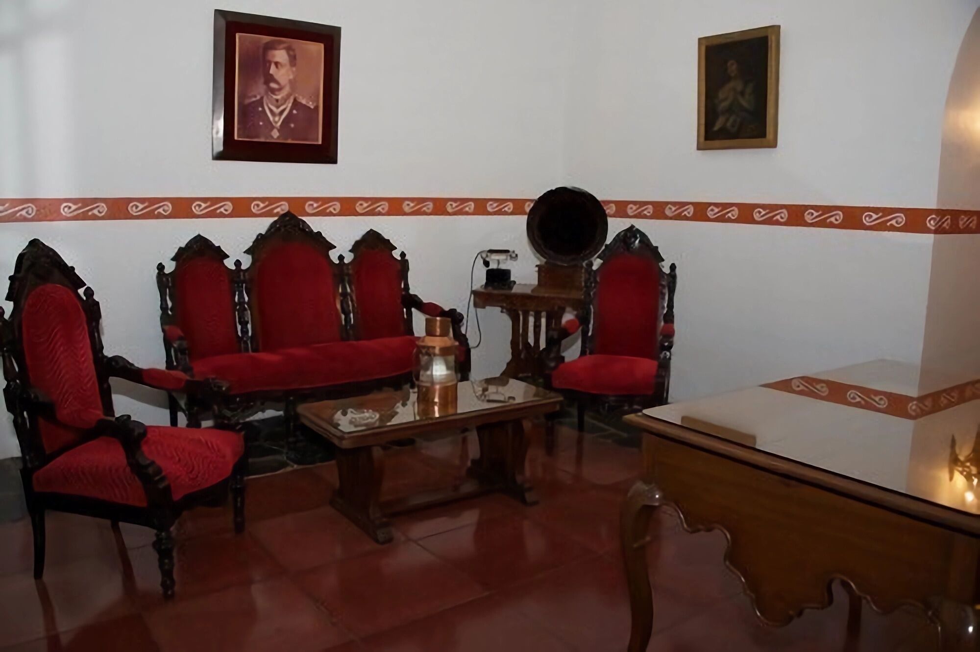 A room with a wooden table, two red upholstered chairs, a red sofa, and a small side table with a lamp.