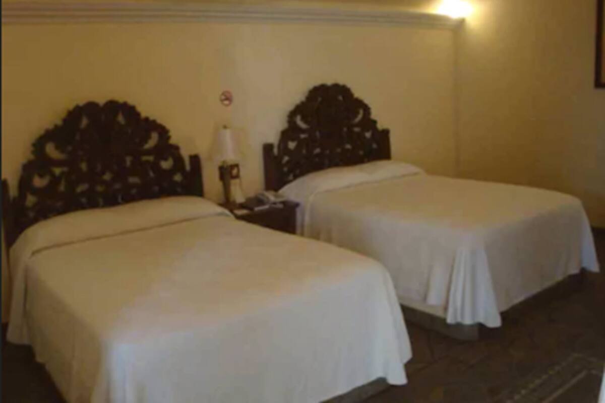Two single beds with wooden headboards, a nightstand with a lamp, and a wall-mounted air conditioner.