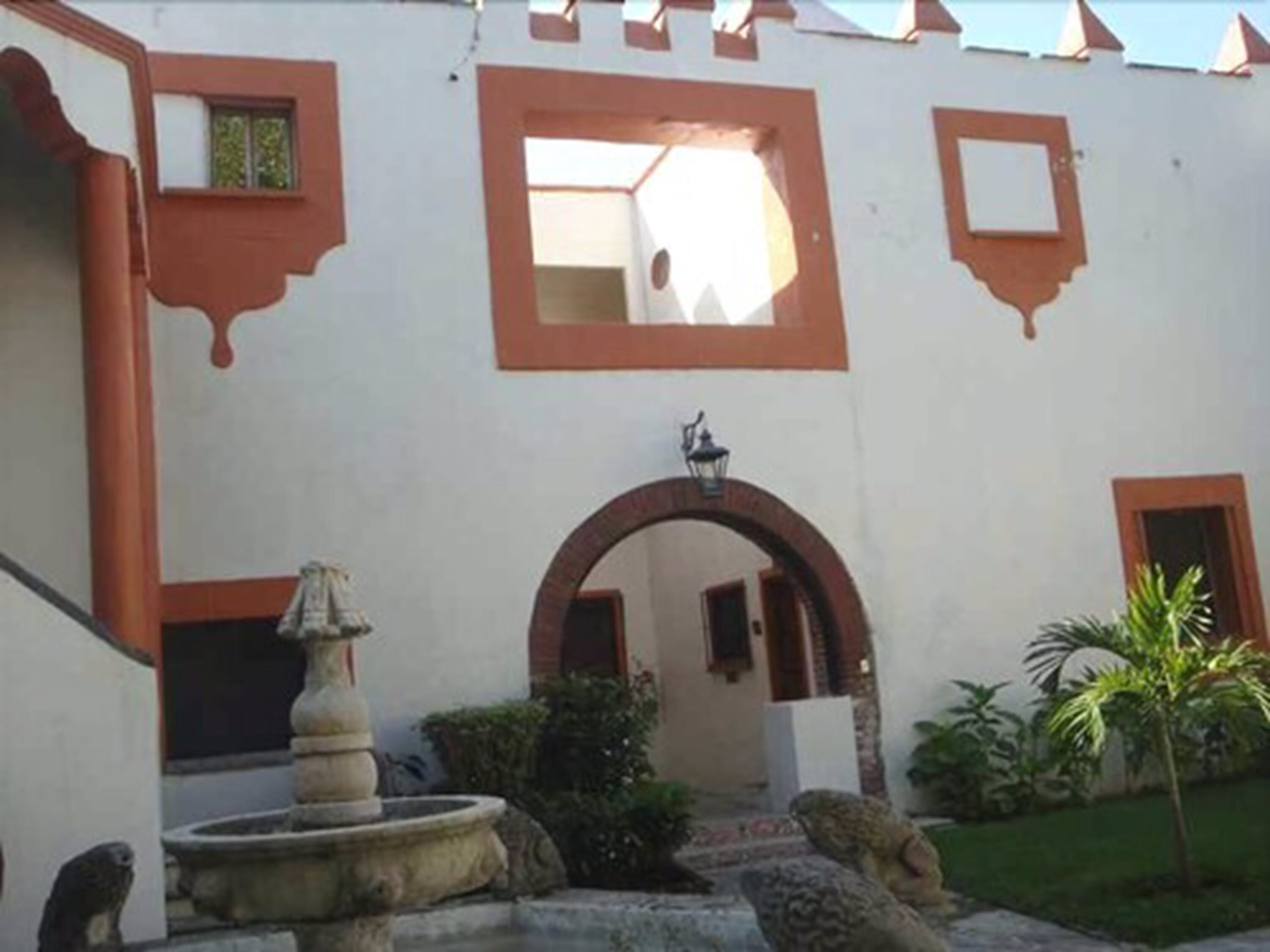 Un patio con una fuente, leones de piedra y una pequeña palmera.