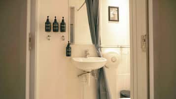 Un baño con lavamanos, cortina de ducha y tres botellas de productos para el cuidado personal y refrescos en la pared.