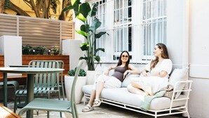 Un espacio al aire libre con un sofá blanco, sillas verdes y una mesa redonda.