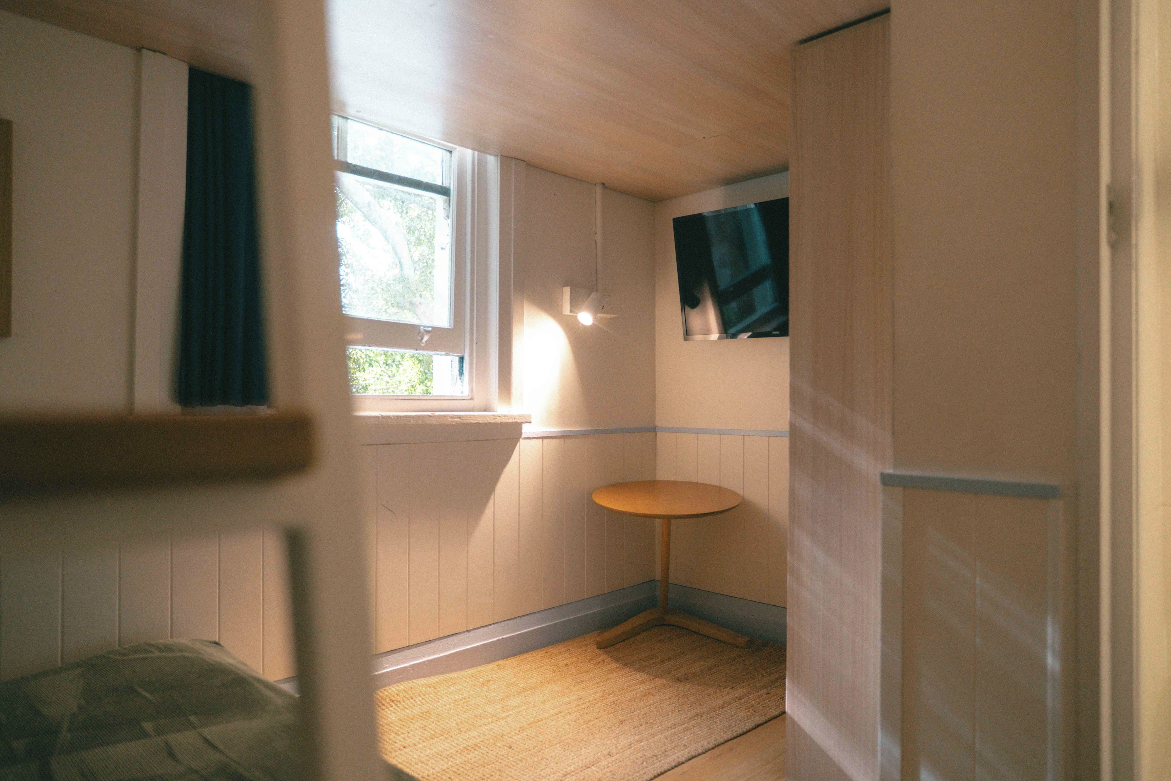 A small, narrow room with a window, a wall-mounted shelf, and a door.