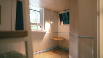 A small, narrow room with a window, a wall-mounted shelf, and a door.