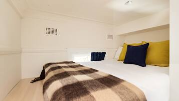 A hotel room with a large bed, white walls, and a ceiling with a recessed light fixture.