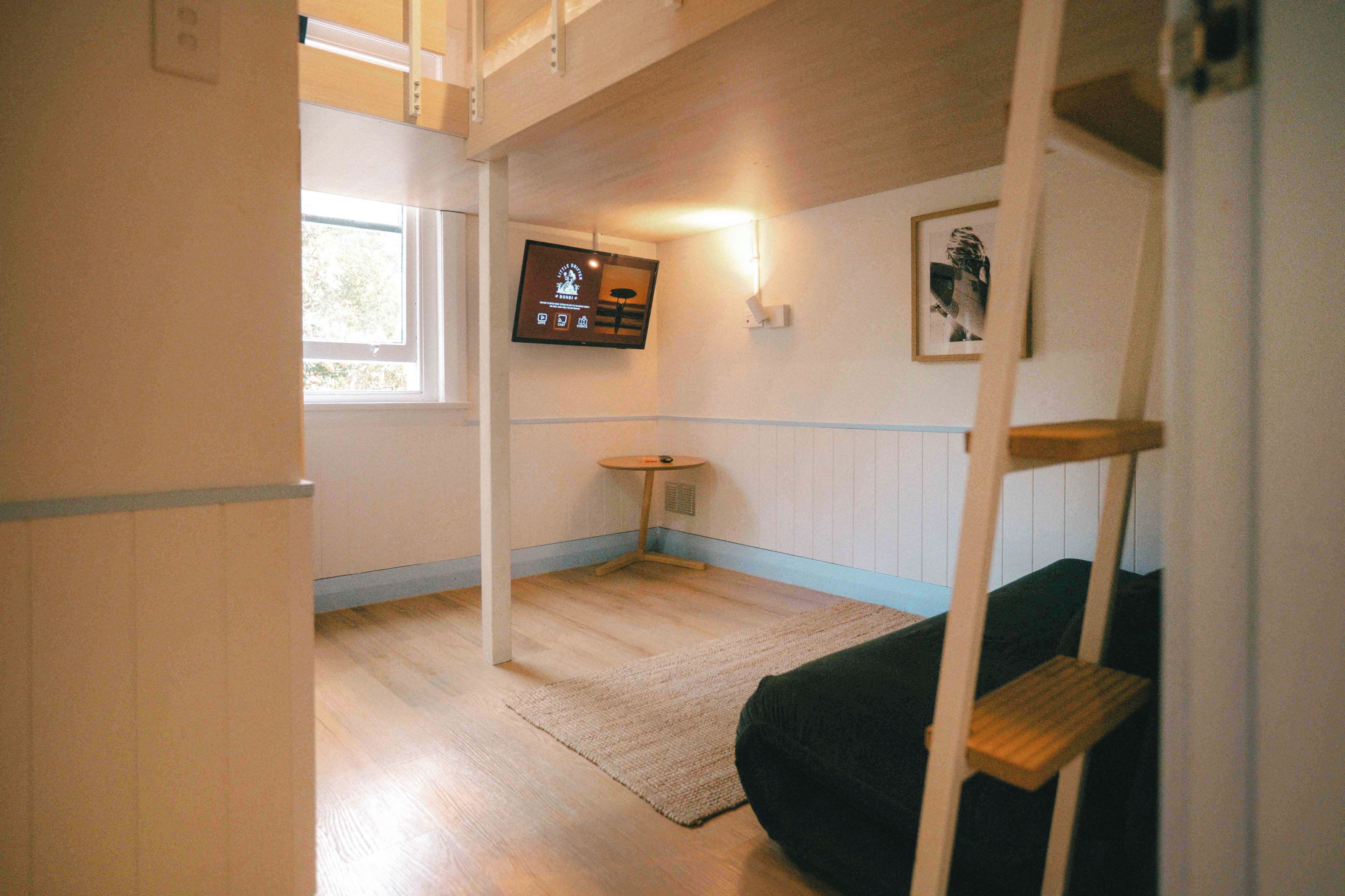 A room with a bunk bed, a small table, a television mounted on the wall, and a framed picture.