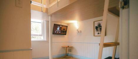 A room with a bunk bed, a small table, a television mounted on the wall, and a framed picture.