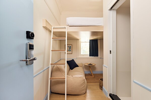 Habitación pequeña con una cama litera, un sofá, una mesita y una puerta con cámara de seguridad.
