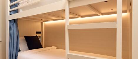 A bunk bed with a lower bunk and a single bed. There is a curtain on the lower bunk, and a pillow on the single bed.