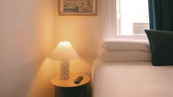 A hotel room with a bed, a nightstand with a lamp, a remote control, and a window with curtains.