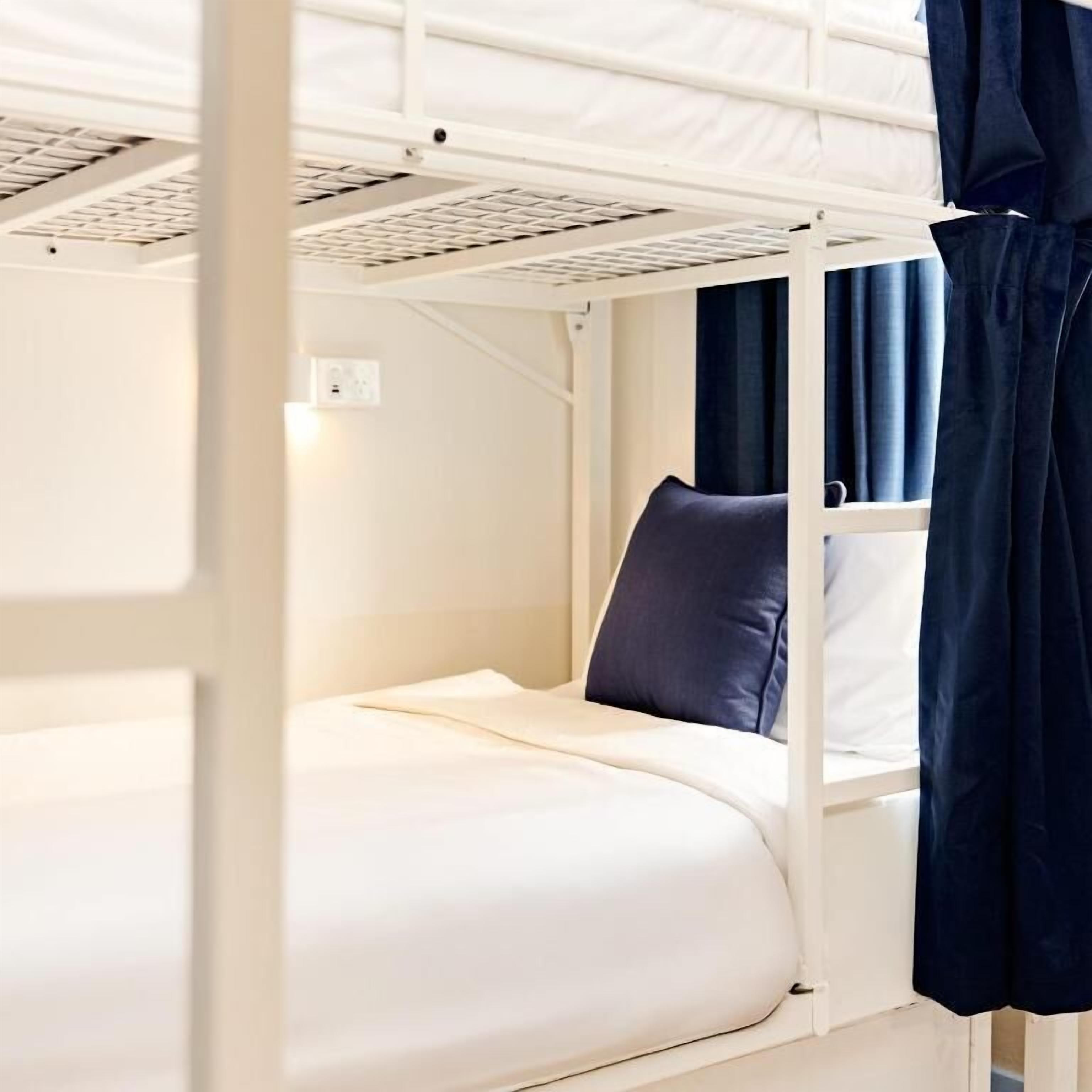 Un lit superposé avec une structure blanche, un lit simple en bas et un rideau sur le côté droit.