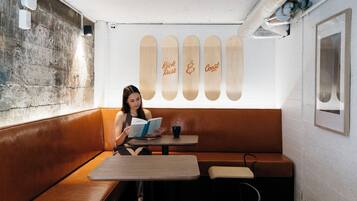 A woman reading a book at a table in a cafe with wooden benches and a wall with skateboards.
