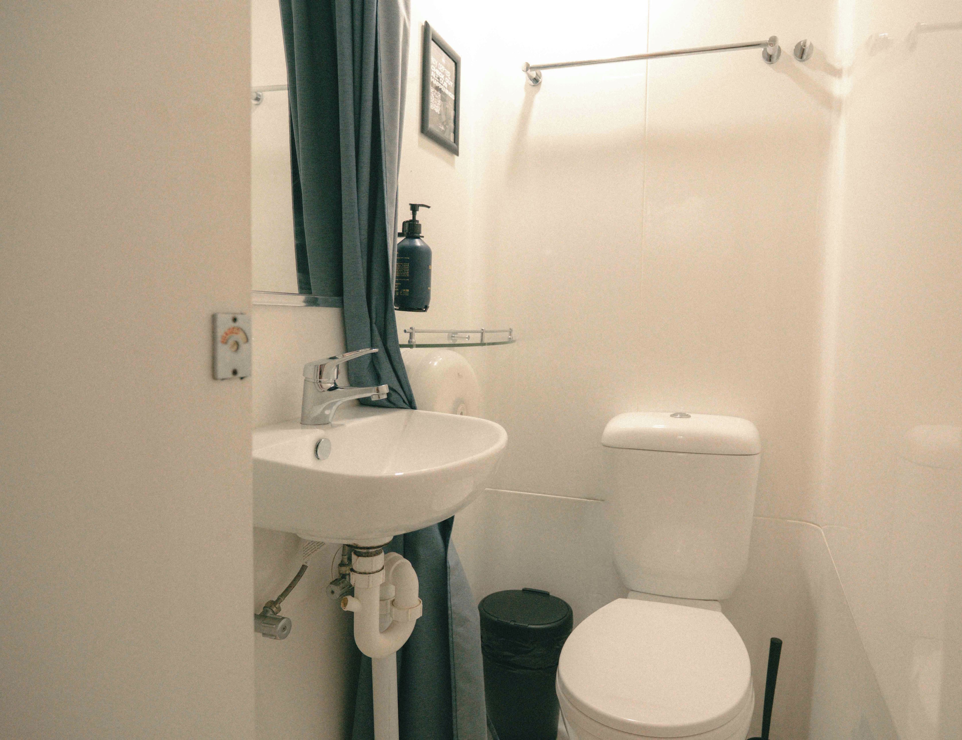 A bathroom with a white sink, a toilet, and a black trash bin.