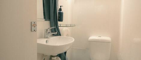 A bathroom with a white sink, a toilet, and a black trash bin.