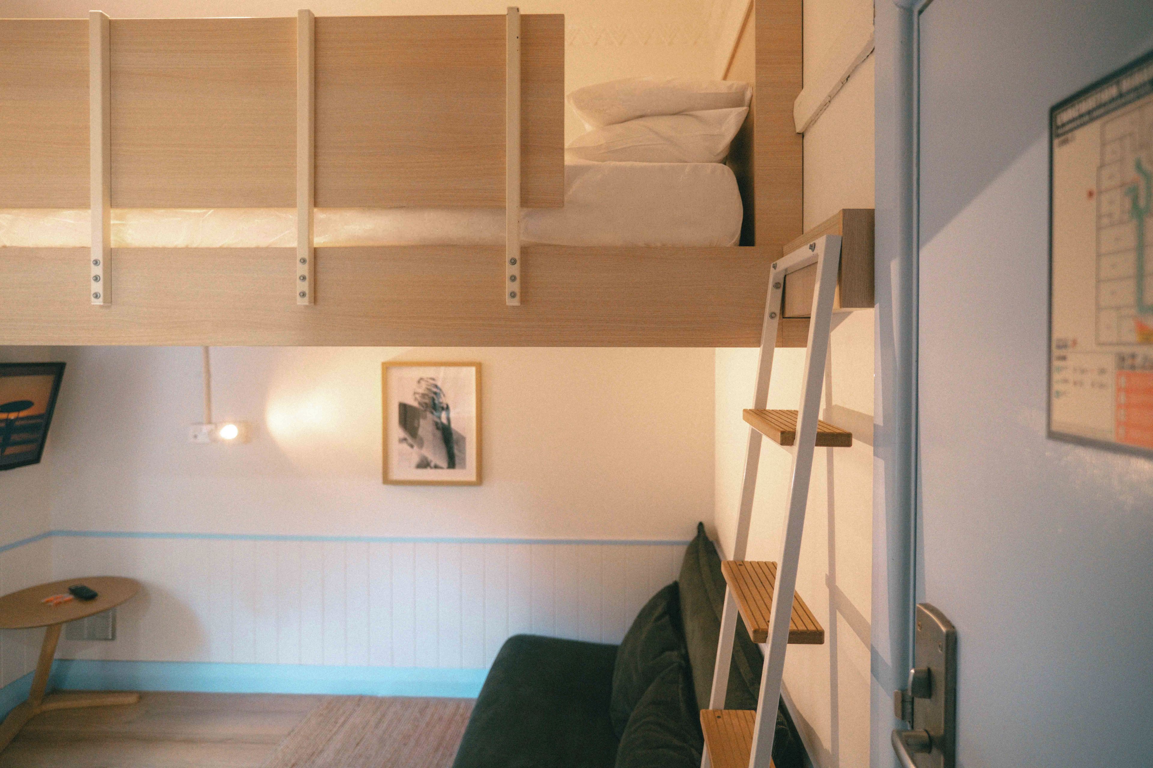 Ein Zimmer mit einem Etagenbett, einem kleinen Tisch, einem Stuhl, einem gerahmten Bild an der Wand und einer Treppe.
