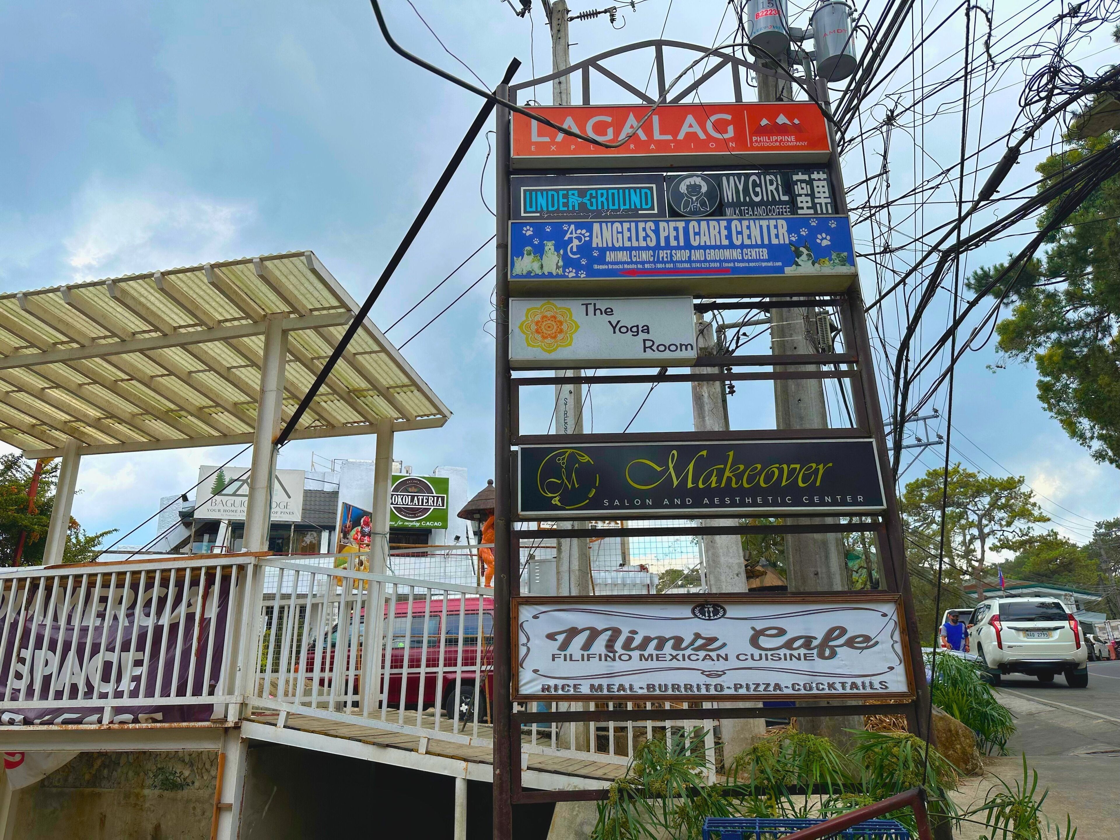 A signpost with various business advertisements including a pet care center, a cafe, and a yoga room.