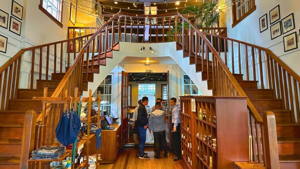 A wooden staircase with a view of the interior, including a desk area with various items and a bookshelf.