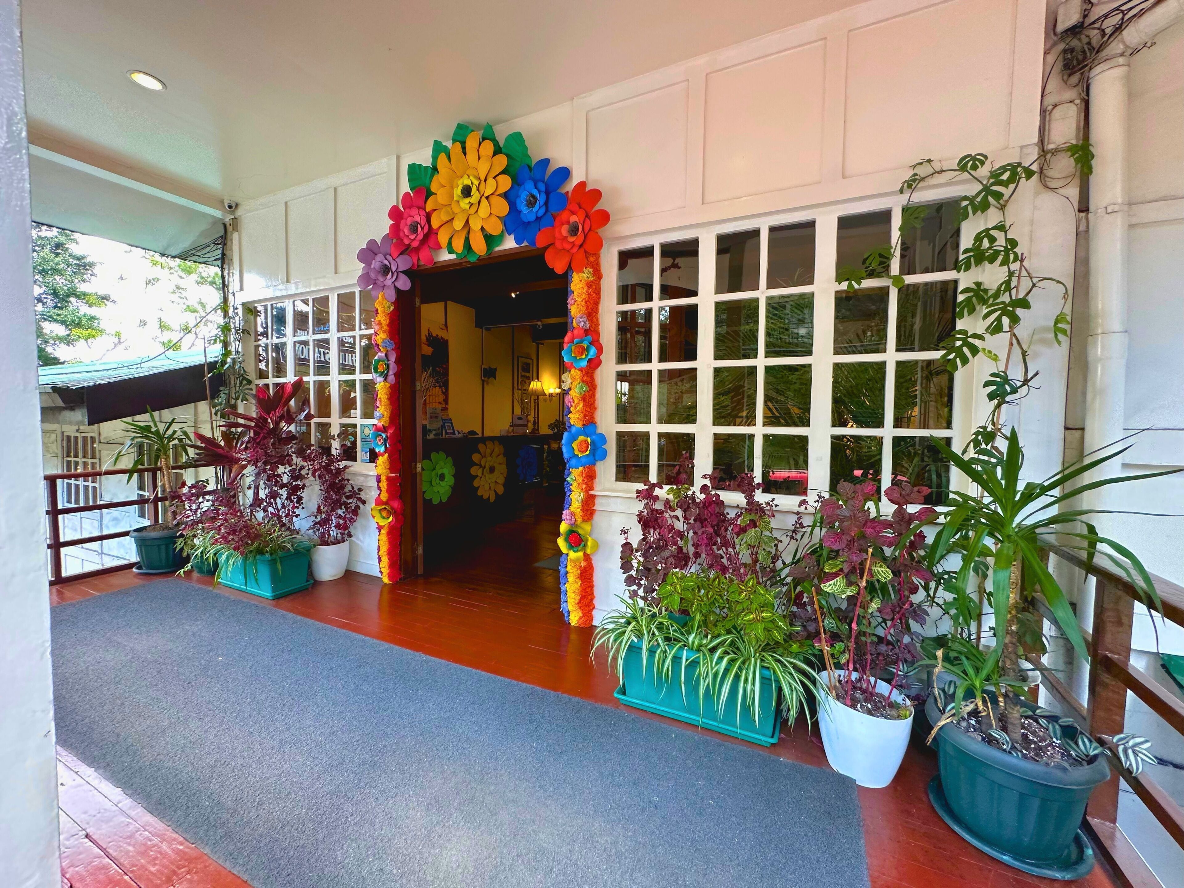 A hotel entrance with a colorful flower archway, potted plants, and a view of the interior.